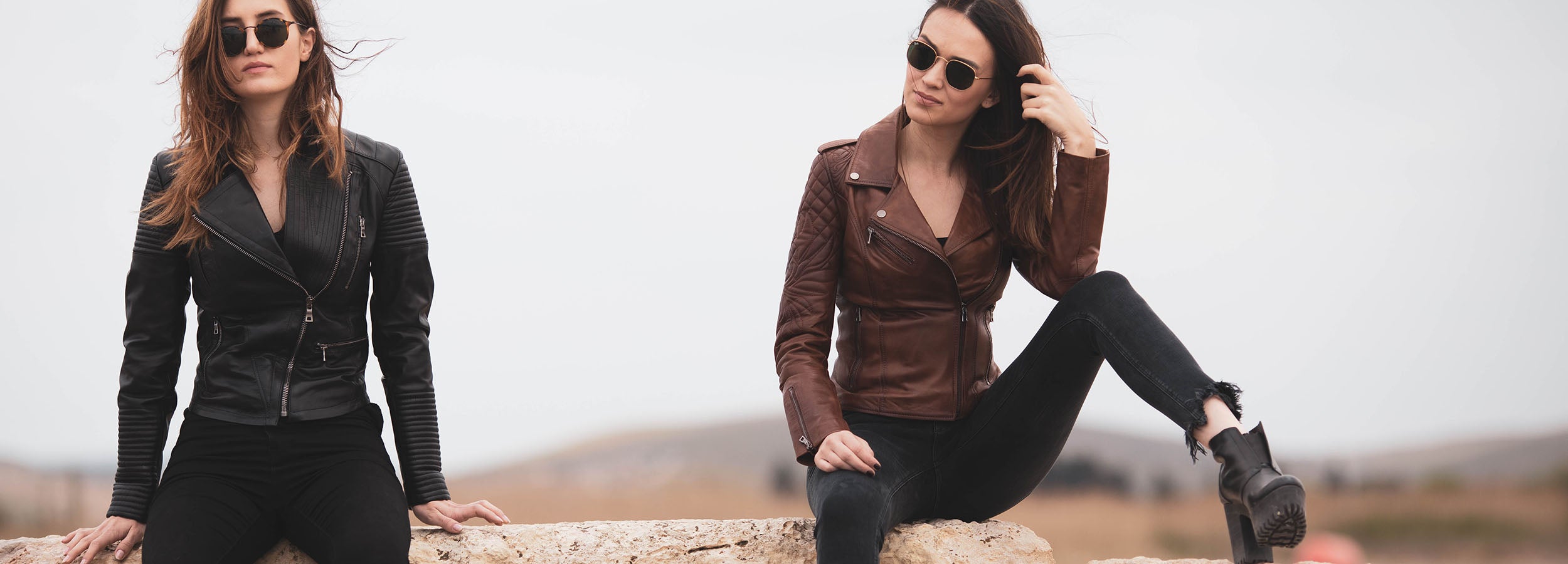 two women in leather jacket sitting on rock posing