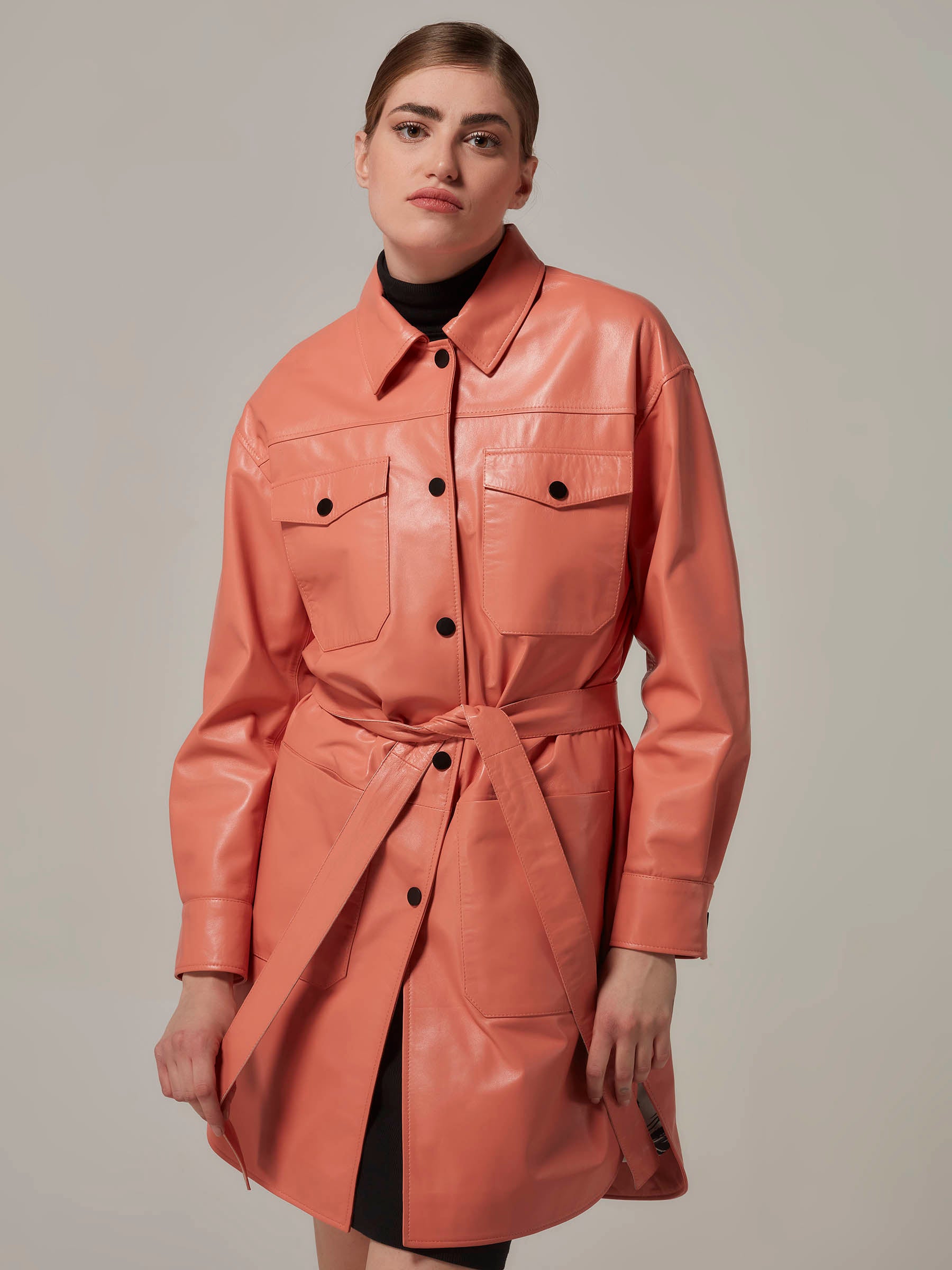 A woman wearing a soft orange leather shirt jacket with a standing collar, featuring front pockets and a belt.