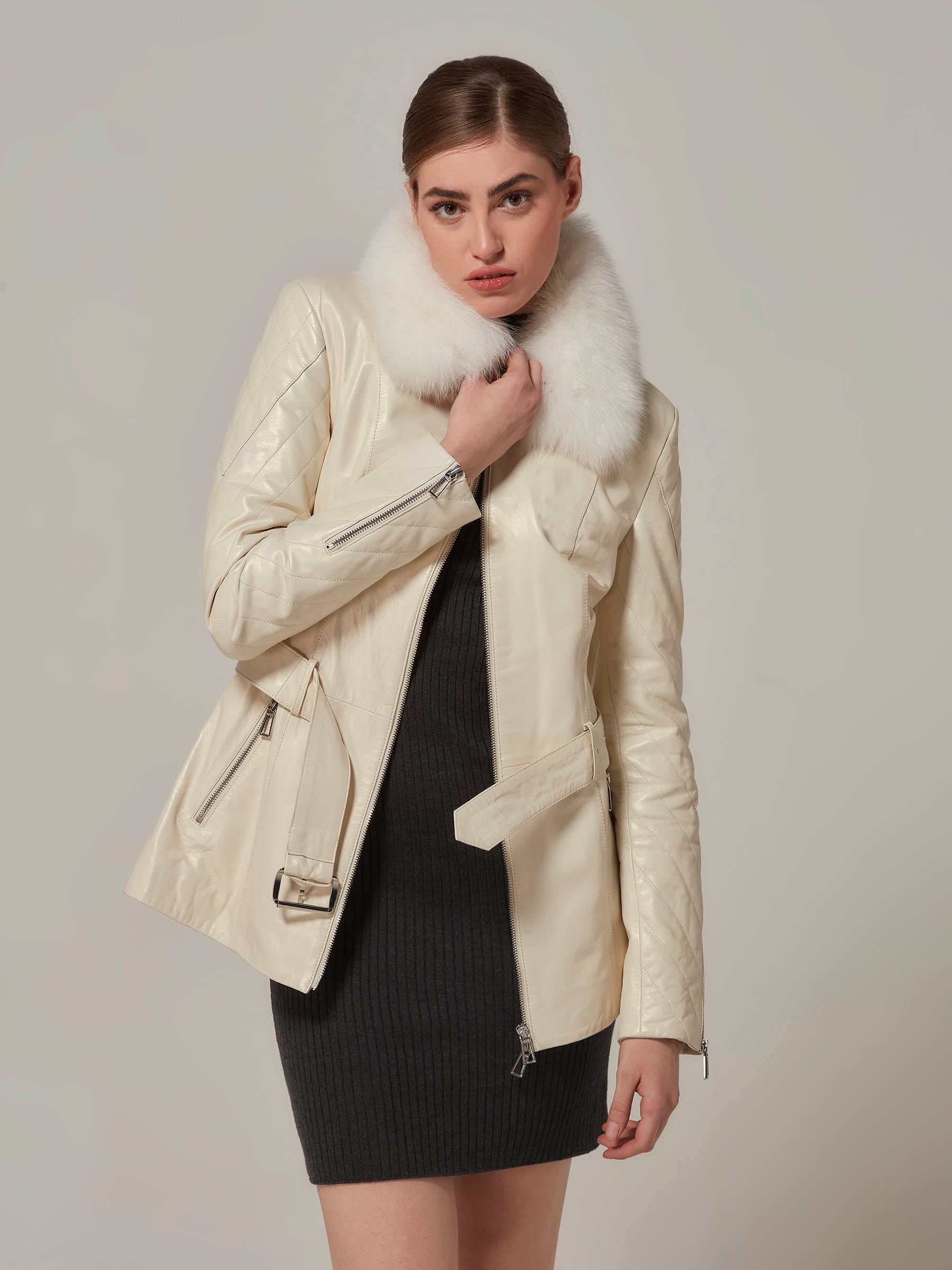 A woman wearing a white leather motorcycle jacket with a luxurious white fox fur collar, featuring quilted details on the shoulders. Her Jacket front zipper wide open.