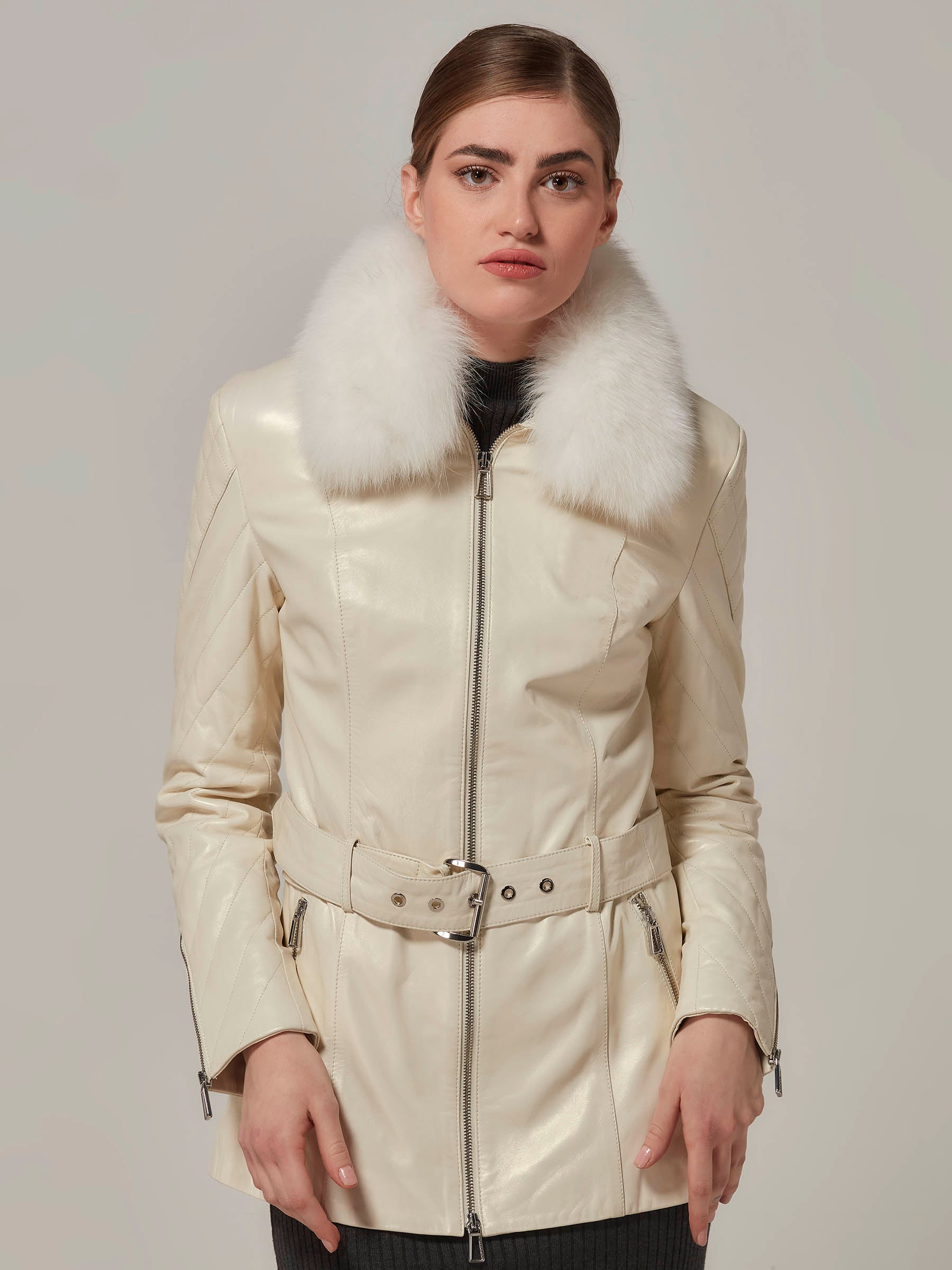 A woman wearing a white leather motorcycle jacket with a luxurious white fox fur collar, featuring quilted details on the shoulders.